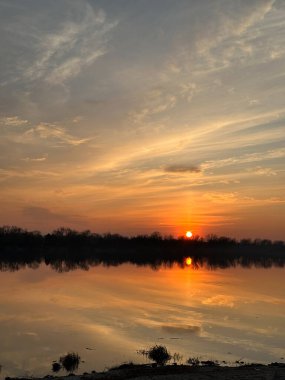 Sakin bir nehrin üzerinde güzel bir günbatımı Canlı Akşam Gökyüzünü yansıtıyor
