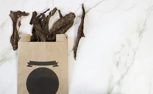 Dried meat in a recycled paper bag, healthy treats used for training or training a pet, especially dogs and cats, on a marble background