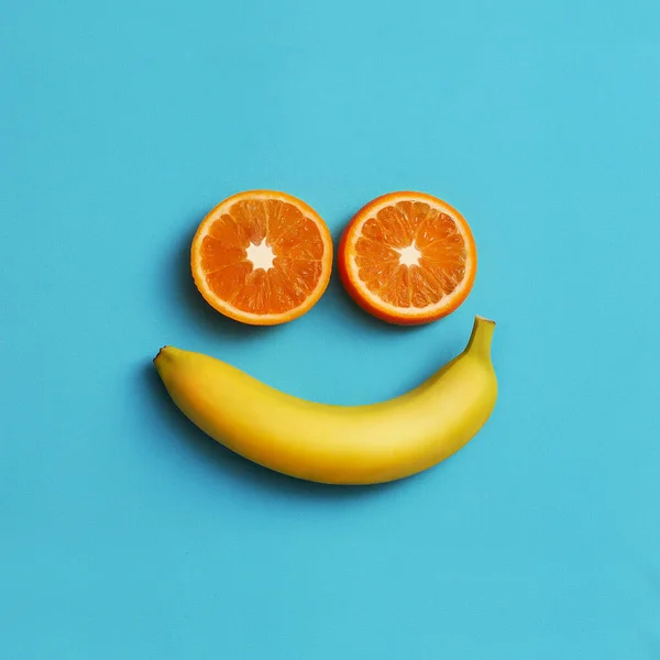 Creative face made of banana and oranges on a blue background