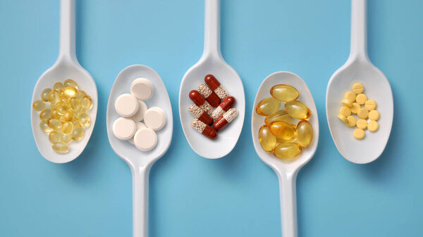 Tablets, capsules, dietary supplements, vitamins on white spoons. Medical background with pills