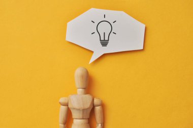 Kafasında yanan bir ampul olan tahta bir adam. Bir insanın yaratıcı fikrinin sembolü.