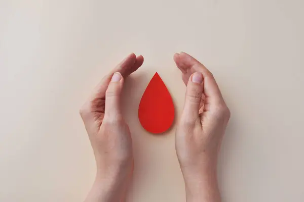 Kan bağışı veya sağlık konsepti için kırmızı kan damlası sembolü tutan eller.