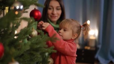 Beyaz, tatlı bir kız, oturma odasında Noel ağacı süslemesine yardım ediyor. Güzel bir kızın portresi. Annesine süsleme yapmak ve terk etmek için çabalıyor.