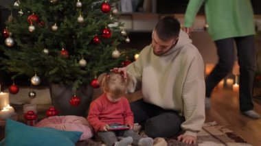 Sevgi dolu genç bir baba, sevimli küçük kızının saçlarını karalayıp telefonda çizgi film izliyor ve anne Noel hediyesini getiriyor. Curios Kafkasyalı kız yeni yıl hediyesinde fiyonku yırtıyor