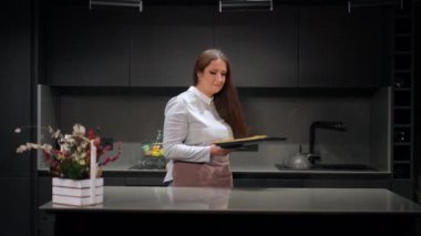 Beyaz, iri yarı ev hanımı mutfağa dönüyor. Masaüstüne lezzetli hamur işleri kokulu tatlı kokulu bir tepsi koyuyor. Tatmin olmuş genç bir kadının portresi evde lezzetli yemekler pişiriyor.