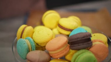 Çok renkli Fransız kurabiyeleriyle yakın çekim tepsisi ve tatlı pastayı ağır çekimde yerleştiren kadın eli. İçerideki beyaz bayanın nefis renkli tatlısıyla tanınmaz hale geldi.