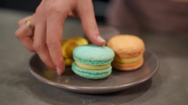 Kapalı renkli Fransız kurabiyeleri tabakta, kadın eli bir kurabiye ısırarak tatlıyı geri koyuyor. İçerde lezzetli hamur işleri yiyen tanınmayan bir kadın.