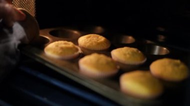 Fırından yavaş çekimde çıkan fırınlanmış keklerle yakın çekim tavası. Tanımlanamayan beyaz bir kadın mutfakta lezzetli pastalar pişiriyor. Şekerleme ve mutfak.