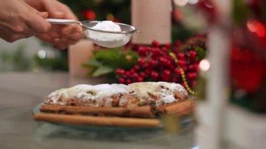 Kapalı alandaki geleneksel Noel pastasına yavaş çekimde toz şeker serpiştirin. Tanımlanamayan Kafkasyalı kadın yeni yıl tatlısını süslüyor evde tatil arifesinde.