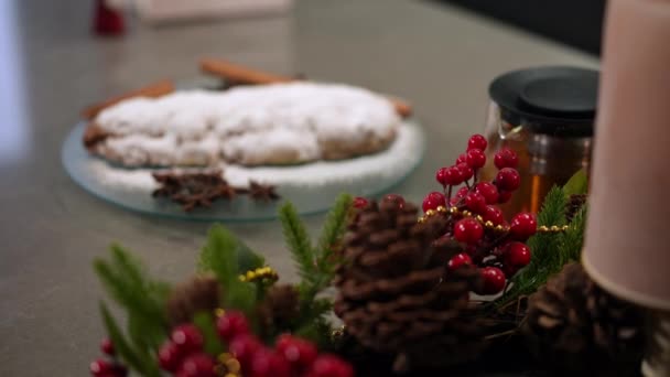 緑のモミの木のパイプコーンからプレート上の伝統的なクリスマスケーキまでのラックフォーカス 屋内のテーブルの上で新年の装飾と甘いデザート — ストック動画