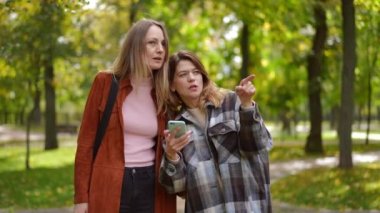 Sonbahar parkında akıllı telefondan ayrılırken online harita uygulaması kullanan kendine güvenen iki beyaz kadının portresi. Güneşli bir günde ağır çekimde uzaklaşan güzel, zayıf arkadaşlar yol güzergahını seçiyor.