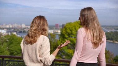Arka planda iki mutlu genç kadının yavaş çekimde el kaldırması arka plandaki bulanık şehir şehrine hayran hayran hayran hayran hayran kalmaları. Güneşli bir sonbahar gününde Kiev şehir parkında Kafkas dostları