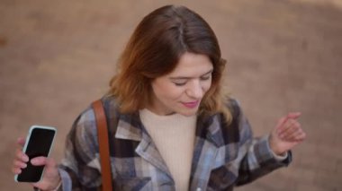 Sonbahar parkında kaldırım kenarında ağır çekimde dans eden rahat mutlu kadın. Dertsiz tasasız, beyaz, güzel bir bayanın açık havada eğlenirken gülümsemesinin yüksek açılı portresi.