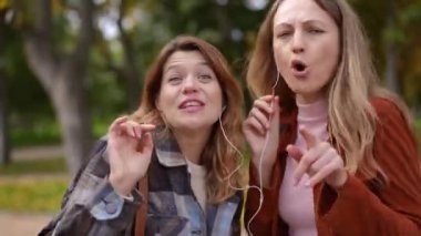 Güz parkında hobisinin keyfini çıkarırken kameraya bakarak somurtan iki neşeli kadının portresi. Neşeli Kafkas arkadaşlarının ön görüntüsü. Hafta sonları dışarıda müzik dinlerken eğleniyorlar.