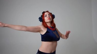 Kendine güvenen bir kadın göğsünü sallıyor. Kalçaları ve elleri ağır çekimde göbek dansı yapıyor. Gri arka planda Konsantre Kafkas dansçısı