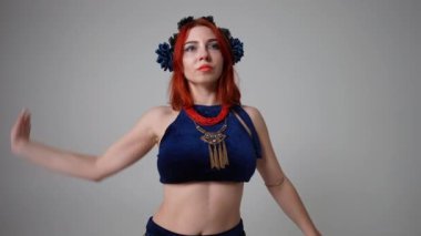 Genç ve güzel bir dansçı göbek dansı yaparken yüzünü çeviriyor. Canlı kamera yaklaş ve gri arka planda dans eden yetenekli, kendine güvenen beyaz kadın olarak yakınlaş.