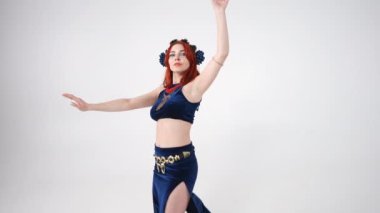 Kendine güvenen, gülümseyen, kalçalarını ve göğüslerini sallayan genç bir kadının Orta Doğu dansına odaklan. Beyaz arka planda yavaş çekimde dans eden beyaz tenli ince dansçı portresi.