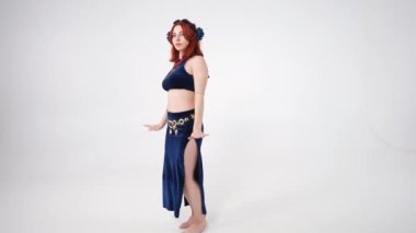 Şehvetli, genç, zayıf bir kadın göğsünü ve kalçalarını sallıyor ve beyaz arka planda ağır çekimde dönüyor. Beyaz tenli yetenekli dansçının portresi kameraya bakıyor ve poz veriyor.