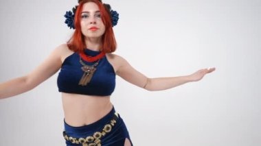 Kameraya bakarak göbek dansı yapan güzel kızıl saçlı beyaz kadın portresi. Beyaz arka planda yavaş çekimde poz veren kendine güvenen zayıf bayan.