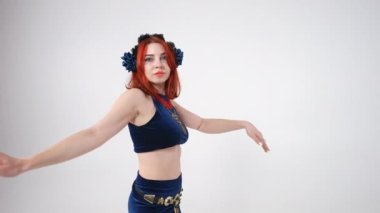 Güzel, genç, zayıf bir kadın kameraya bakıyor göbek dansını seyrediyor ağır çekimde dönüyor. Beyaz arka planda sahne alan muhteşem beyaz dansçı görüntüsü.