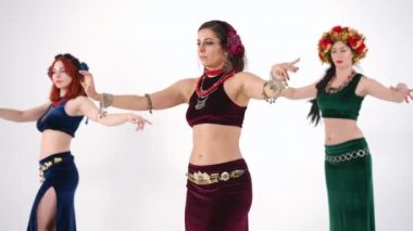 Üç zayıf kadın ağır çekimde esnek vücutları hareket ettiriyor ve beyaz arka planda dans ediyorlar. Orta Doğu dansı yapan özgüvenli beyaz dansçılar el kaldırıyor.