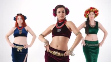 Beyaz arka planda yavaş çekimde göbek dansı yapan üç çekici kadın. Kameraya bakarak dans eden beyaz dansçıların ön manzara portresi.