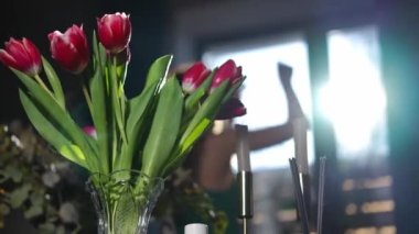 Güneş ışınlarıyla arka planda dans eden bulanık zayıf bir kadınla yakın plan lale demeti. İçerideki vazoda çiçekler, mutlu beyaz bir bayanın evinde keyfine bakıyor.