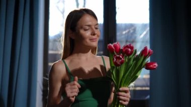 Gün ışığında lale buketiyle dans eden mutlu genç bir kadının orta boy portresi. Memnuniyetle Kafkasyalı güzel bayan. Evde güneş ışığında çiçekler. Yavaş çekim