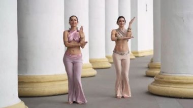 Kendine güvenen yetenekli kadınların Hint dansı yapıp aynı anda kalça sallamalarına odaklan. Güzel dansçılar şehrin beyaz kolonları arasında dans ederken kameralar yaklaşıyor.