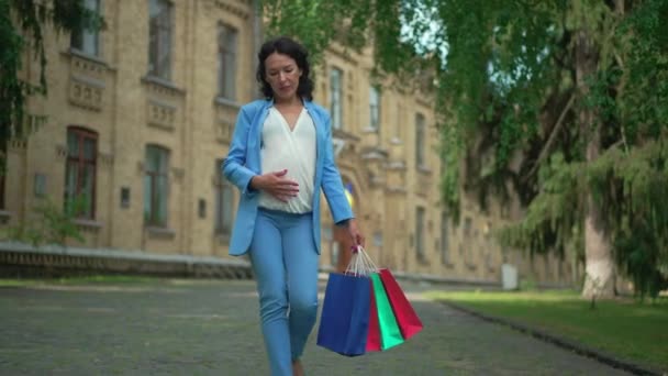 幸せな妊娠中の女性のドリーショットの肖像ショッピングバッグを屋外で愛撫腹笑顔で歩く 白人はブラックフライデーの売り上げで市内を散歩することを期待していました — ストック動画