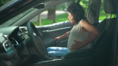Kafkasyalı hamile kadın arabadan yavaş çekimde dışarı çıkıyor. Güzel esmer bayanın yan manzara portresi Yolcu koltuğundan kalkmış karnını tutuyor