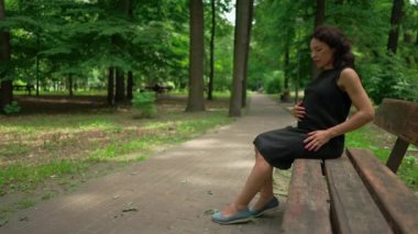 Bacakları ağrıyan ve sırtı ağrıyan hamile bir kadın yaz parkında bankta oturuyor. Güneşli bir günde açık havada dinlenen Kafkas beklentisinin portresi. Yavaş çekim