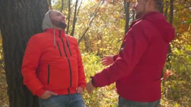 Partnerim öpüşmeye yaklaşırken parkta ağaca yaslanan rahat eşcinsel adam. Açık havada flört eden mutlu beyaz çift portresi Ormanda güneşli bir sonbahar gününün tadını çıkarıyor