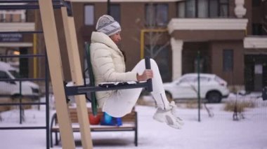 Sıska gülümseyen sporcu kadın dışarıda antrenman yapıyor, bacaklarını kaldırıp başka tarafa bakıyor. Kafkasyalı genç ve güzel bir kadının kış günü spor yapmasına ilham verdi.