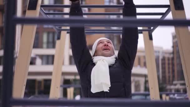 成年白人男子在冬日户外悬挂在运动器材上 积极的运动员在户外运动时的正面形象 健康生活方式概念 — 图库视频影像