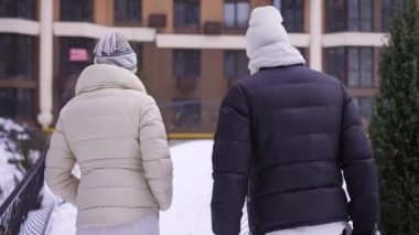 Beyaz erkek ve kadın kışın köprüdeki konuta doğru yürüyorlar. Canlı kamera rahatlamış yetişkin çiftin dışarıda konuşmalarını takip ediyor.