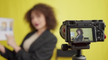 Genç, pozitif bir kadının reklam afişini videoya çekerken gösterdiği video kamera. Kendine güveni olan mutlu, başarılı, beyaz kadın nüfuzlu birinin portresi sarı arka planda video blogu kaydediyor.
