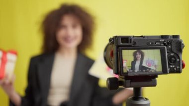 Blog yazarının hediye ettiği yakın plan video kamera görüntüsü ve sarı arka planda konuşan bulanık bir genç kadın. Pozitif çekici esmer Kafkas video blogcusu sürpriz film teklifi