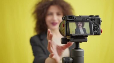 Gülümseyen beyaz bir kadının video kamera ile yakın plan görüntüsü. Vlog 'u kaydeden ayarlar. Sarı arka plandaki güzel kadın blogcu kayda başlıyor. Modern teknolojiler ve sosyal medya