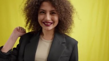 Neşeli, mutlu sosyal medya blogcusu kamerayı el sallayarak açıyor. Sarı arka planda poz veren neşeli beyaz güzel bir kadının portresi vlog çekerken eğleniyor