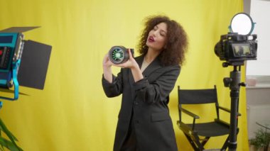 Çekici, beyaz bir kadın video reklam videosu çekmekten bahsediyor. Kendine güvenen güzel kadın blogcunun portresi sarı arka planda profesyonel ekipmanları gözden geçiriyor.