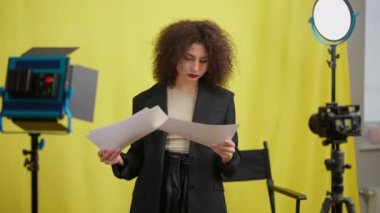 Sarı arkaplanda kamerayla istatistikleri analiz eden zeki bir kadın. Kendine güvenen sosyal medya etkileyicisinin vlog planlamasının orta boy portresi