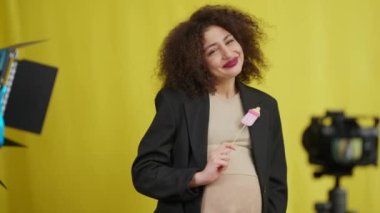 Portrait of happy beautiful woman with paper pacifier caressing pregnant belly filming vlog. Smiling confident Caucasian blogger recording video at yellow background