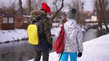 Tracking shot of teenage girl strolling with boy outdoors passing backpack. Loving Caucasian teen couple walking on winter day after school talking enjoying leisure