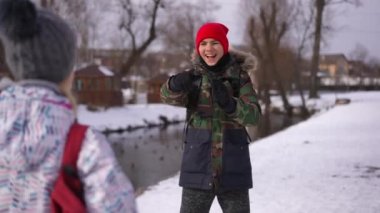 Laughing teenage Caucasian boy making fun of girl running away with backpack. Portrait of handsome teenager mocking as girl running after boy on winter day outdoors