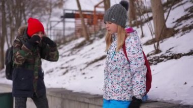 Sad bullied teen schoolgirl standing on winter day outdoors as rude schoolboy laughing gesturing sneering at background. Portrait of depressed Caucasian girl looking at camera with despair