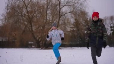 Joyful boy and girl running on white snowy meadow in slow motion leaving. Cheerful Caucasian friends having fun on weekend vacations outdoors. Leisure and lifestyle concept