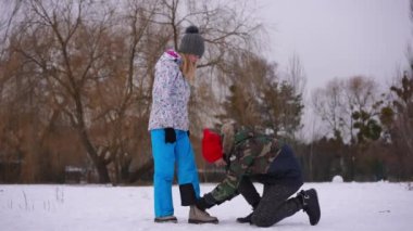 Wide shot smiling teenage girlfriend standing on snow as boyfriend tying shoelaces. Happy loving Caucasian boy and girl holding hands walking away leaving. Romance and first love concept