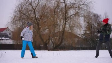 Wide shot carefree cheerful teenage boy and girl playing snowballs laughing out loud outdoors. Happy joyful Caucasian friend having fun on winter day in park. Slow motion