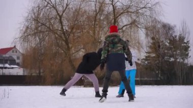 Joyful young Caucasian woman playing with teenage boy and girl on winter day outdoors. Wide shot happy carefree lady having fun with teenagers in park. Slow motion